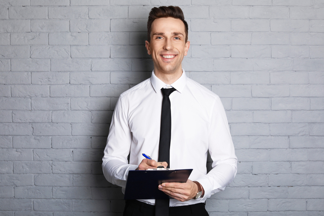 Male real estate agent with clipboard on brick wall background
